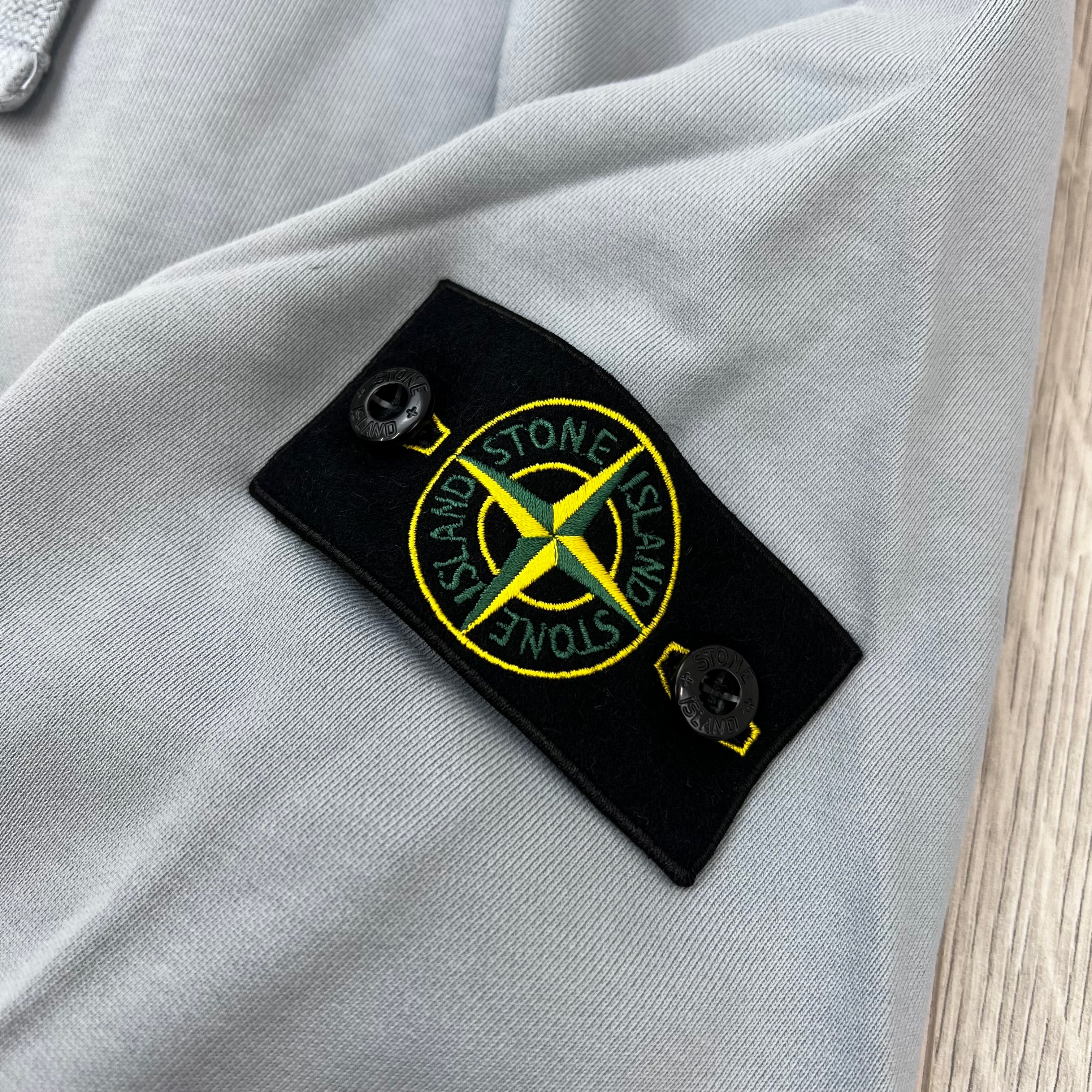 A close view of the badge logo on a Stone Island Pullover Hoodie in Ash Grey. 