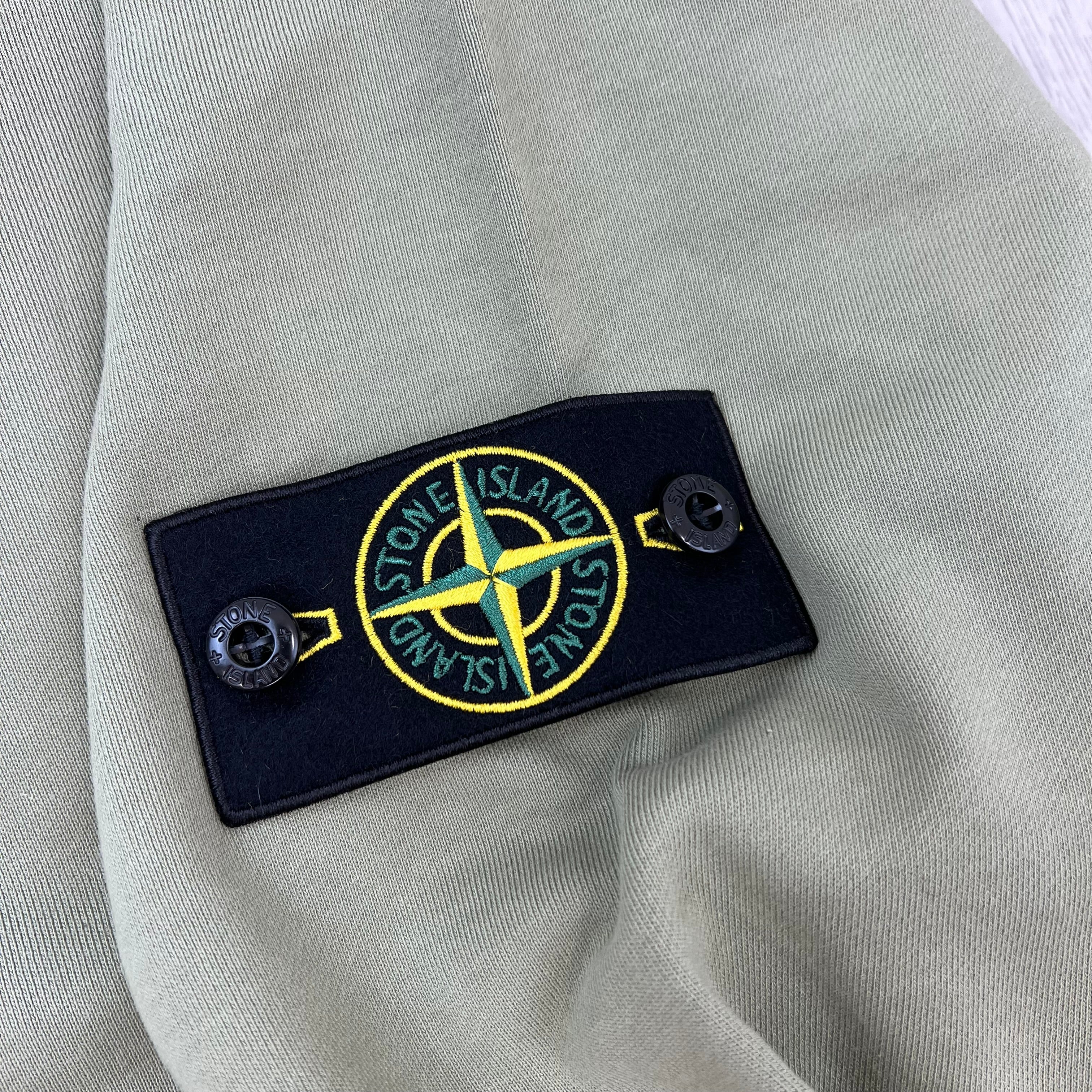 A close up view of the badge logo on a Stone Island Crewneck Sweatshirt in Laurel Green.