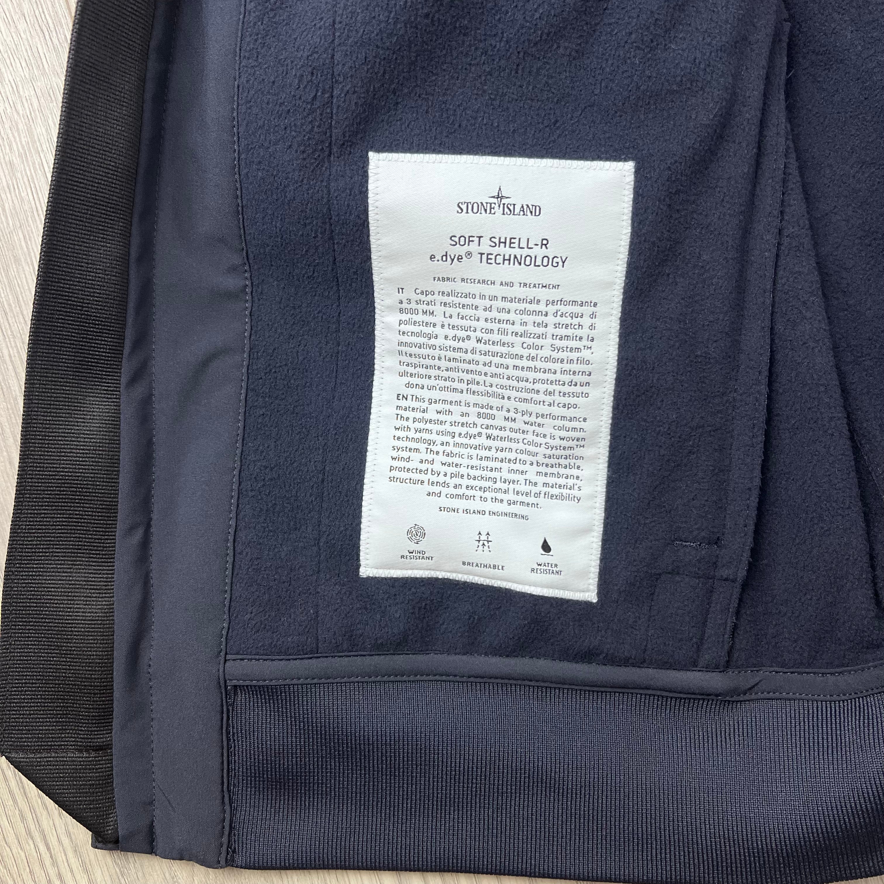 A close up view of the engineering label on the inside of a Stone Island Soft Shell-R_e.dye® Jacket in Navy Blue.